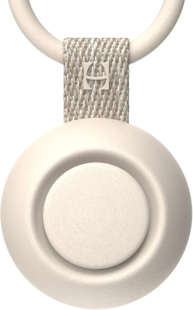 Close-up of a white circular device attached to a textured strap with a metallic ring, embodying the sleek modern aesthetic of baby products for 2025. The strap features a small, square metallic logo, enhancing its minimalist design and light color.