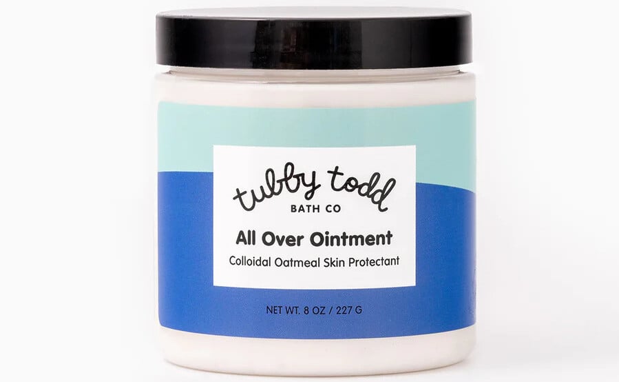 A jar of Tubby Todd Bath Co All Over Ointment, labeled as an essential baby product for 2025, features a blue and green design. This 8 oz (227 g) container is a colloidal oatmeal skin protectant and comes with a sleek black lid, set against a plain white background.