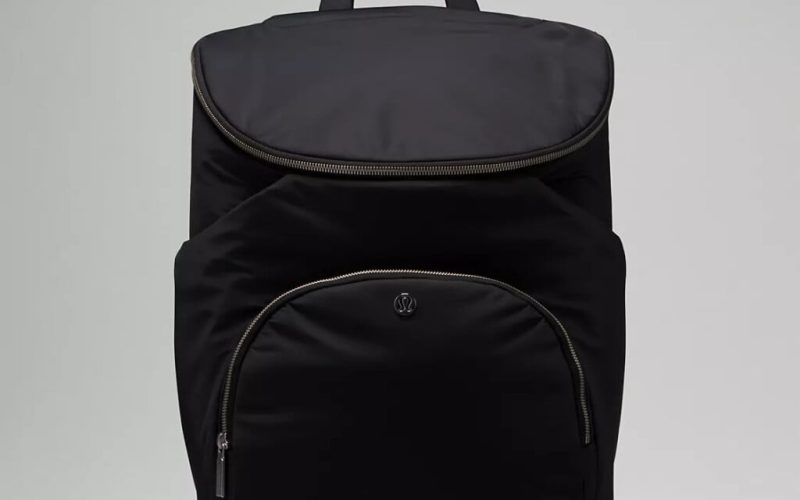 A black backpack designed with the future in mind, perfect for baby products for 2025, features a flap closure and a spacious front zippered pocket. Centered against a plain background, the bags sleek design is completed with a convenient top handle.